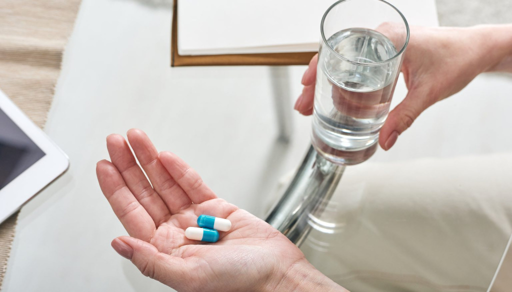 Hands holding pill capsules and a glass of water