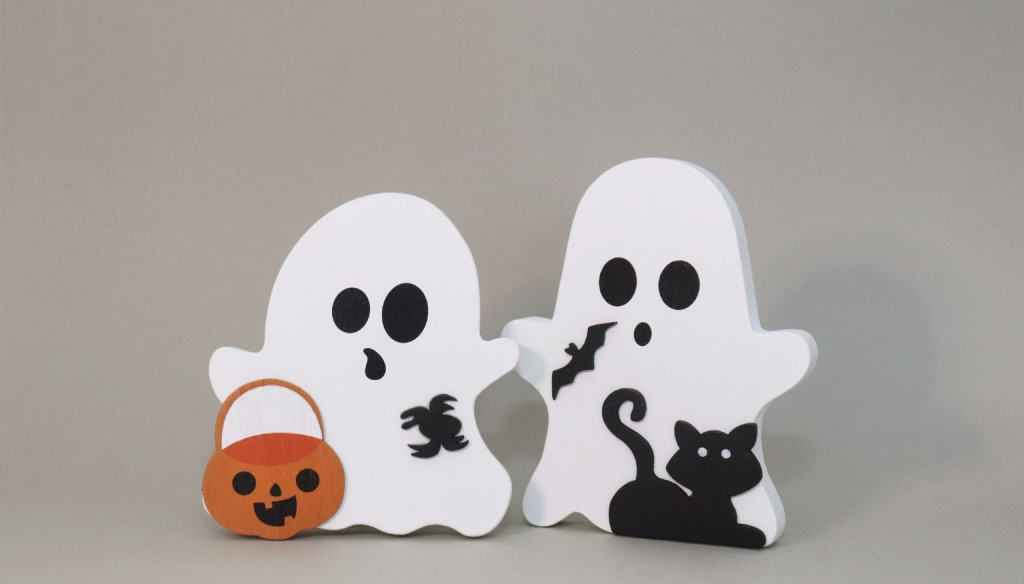 Wooden cutouts of two ghosts with black cat, bats, spiders and pumpkin against a plain background.