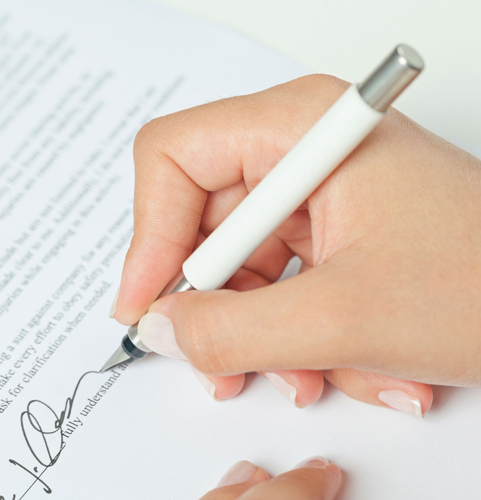 A hand holding a pen and signing a document