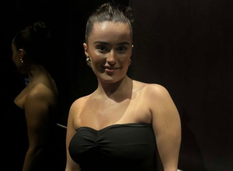 A young woman, Aisha, wearing an off the shoulder black dress and looking at the camera