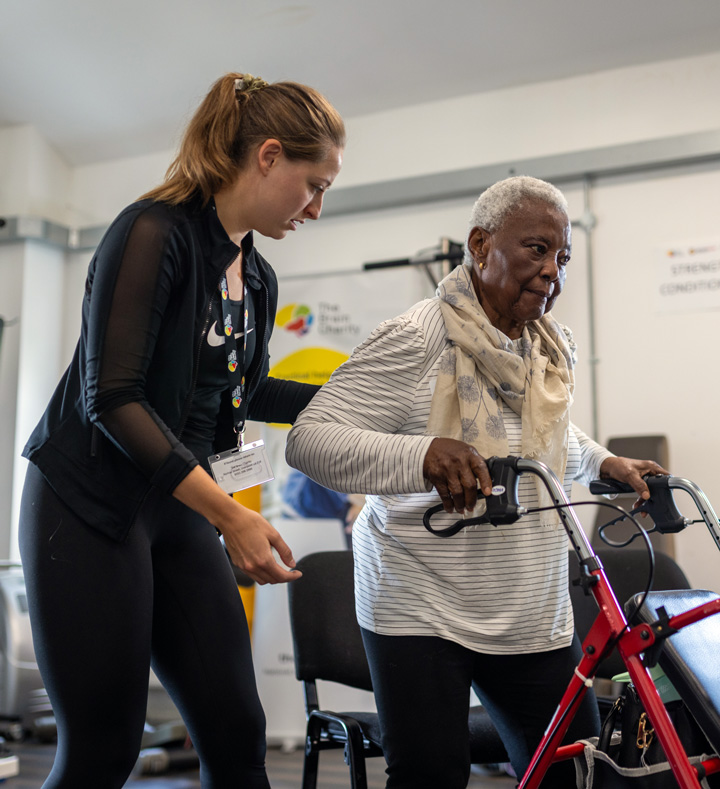 Young woman smiling and guiding another woman with a walker during physiotherapy exercise