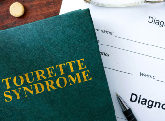 A book on a desk with a diagnosis form, pen and glasses. The title of the book is Tourette syndrome.