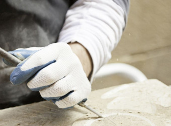 A gloved hand holding a chisel and carving stone