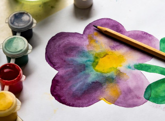 Watercolour painting of a flower surrounded by paint pots on a table