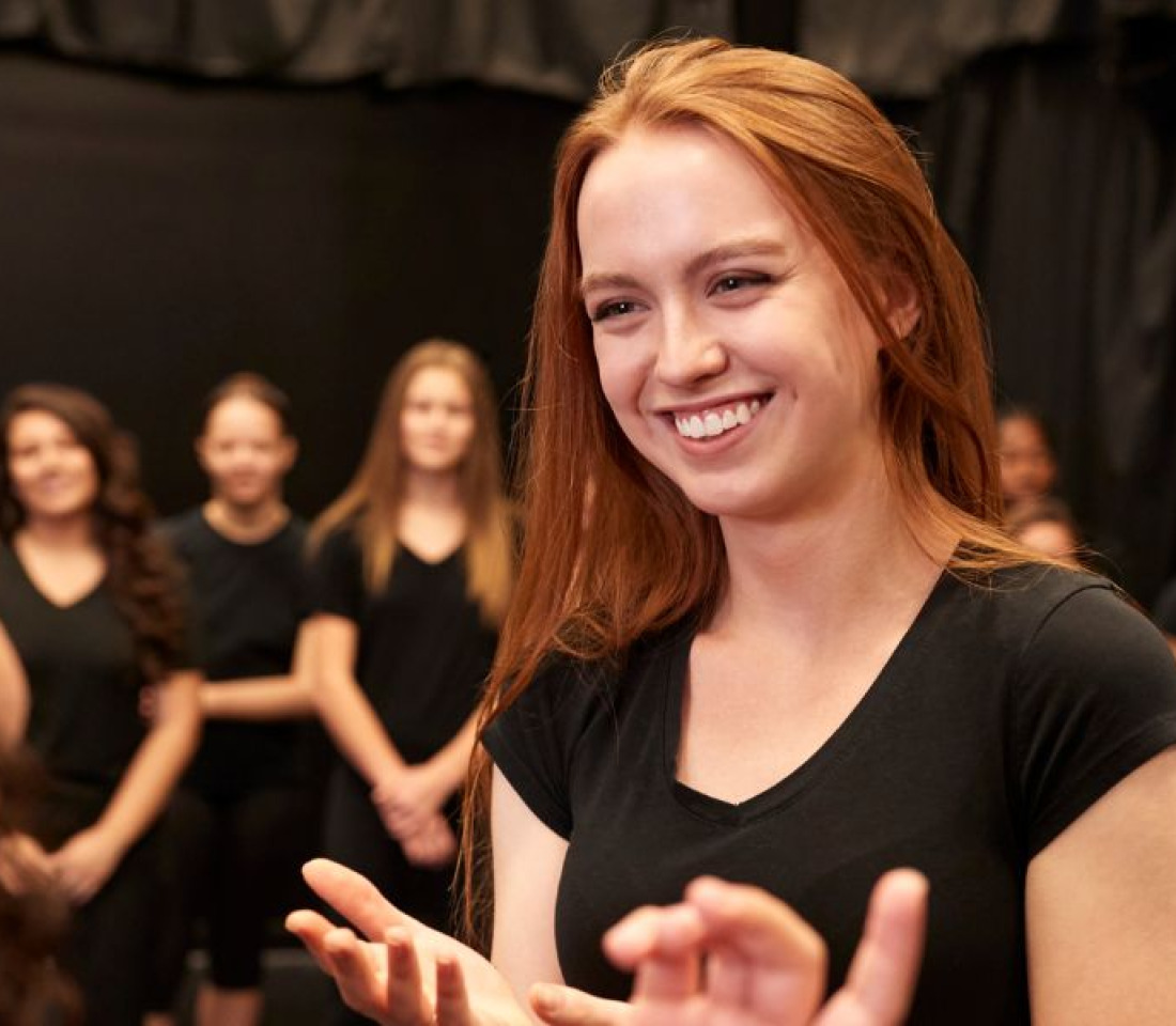 A woman smiling and talking to another at a drama rehearsal