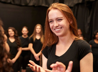 A woman smiling and talking to another at a drama rehearsal