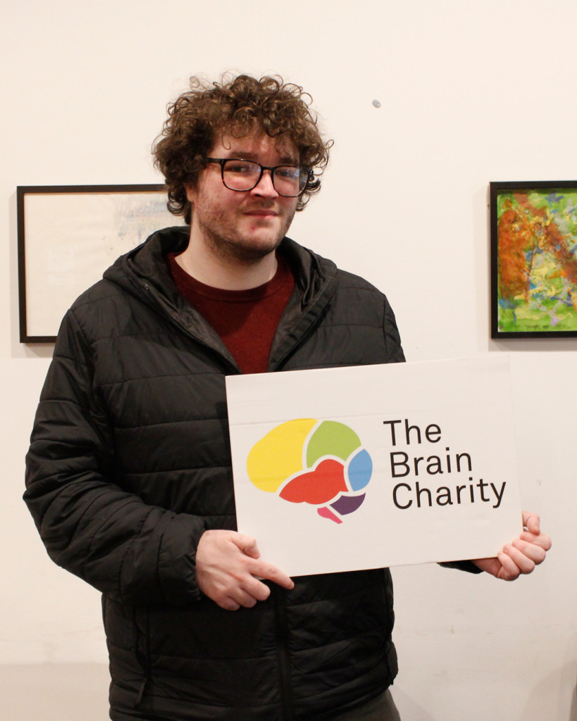 Man (Chris), recipient of our confidence coaching, holding up The Brain Charity logo.
