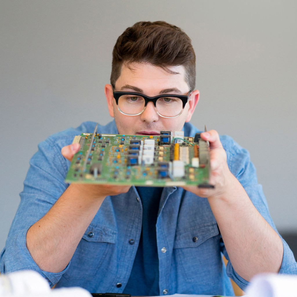 A man in glasses looking at a circuit board