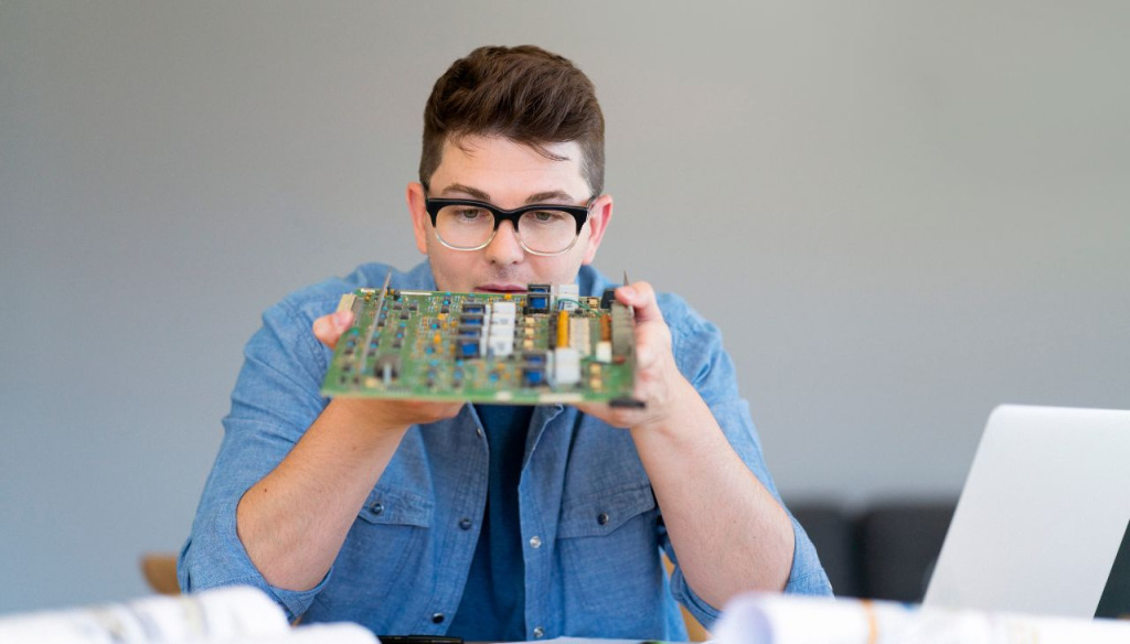 A man in glasses looking at a circuit board