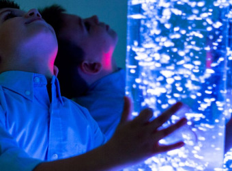 A boy with a bubble tube. His image is mirrored in a wall mirror.