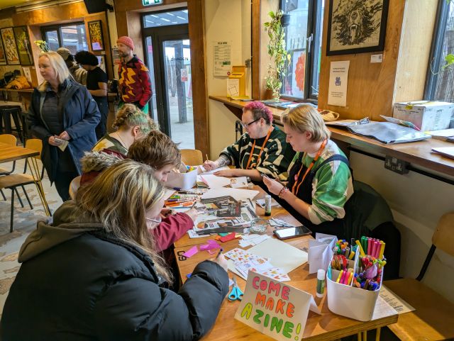 Young People seated at a table taking part in a comics drawing workshop in a bright yellow room, with illustrated posters on the walls