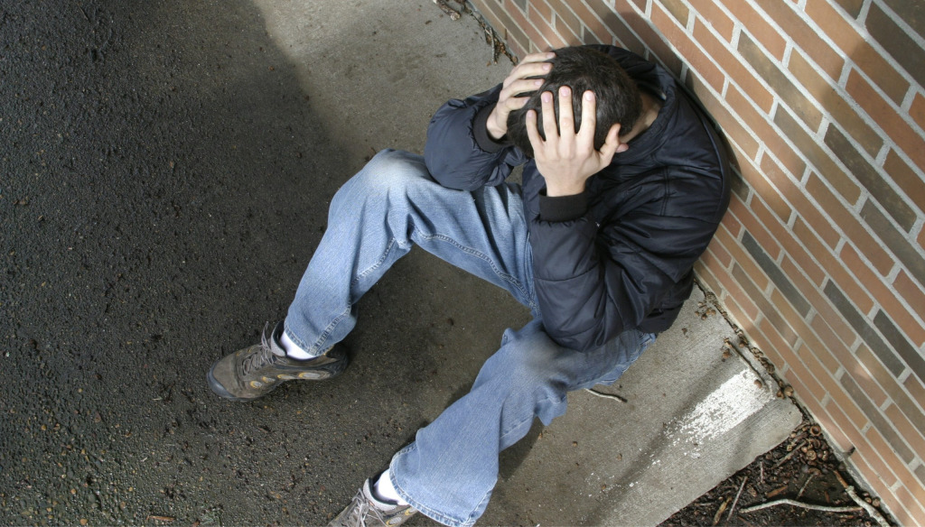 Man in crisis, sitting on pavement with his head in his hands