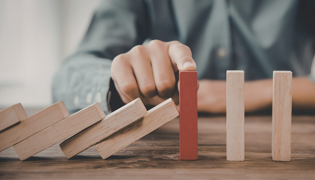 A person stopping a line of dominoes from falling.