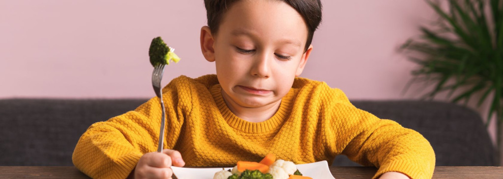 A young boy struggling to eat broccoli