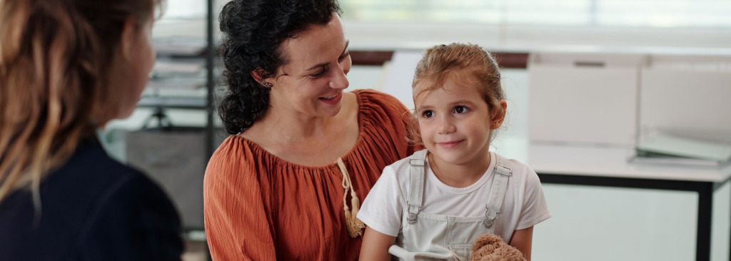 A child sitting on her mother's knee talking to another woman