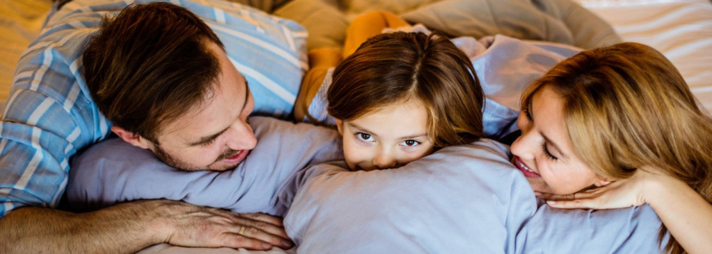 A girl in bed between her parents, they are smiling