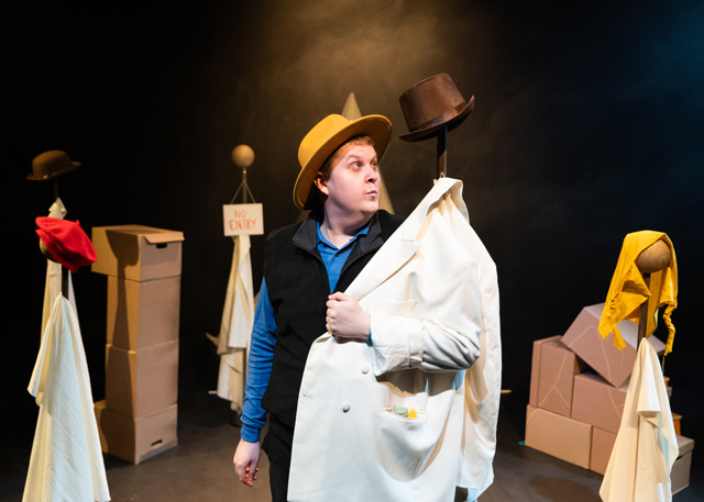 A man on stage in a yellow fedora putting on a jacket