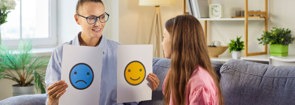 A woman showing a girl cards with a smiling face and a sad face