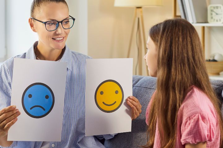 A woman showing a girl cards with a smiling face and a sad face