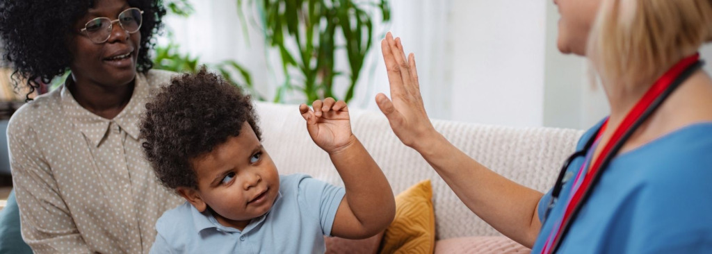 A woman with a child sitting on a sofa with a female doctor. The child is high fiving the doctor.