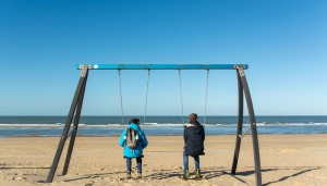 Two people on a swing set by the sea