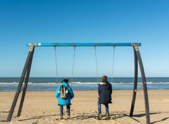 Two people on a swing set by the sea