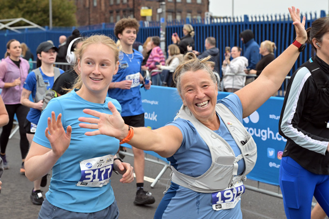 Photo of the race in progress featuring two women, the older woman is smiling at the camera and has arms out stretched. They are both enjoying themselves.