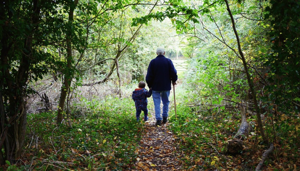 An old, grey haired man walking on a path with a child