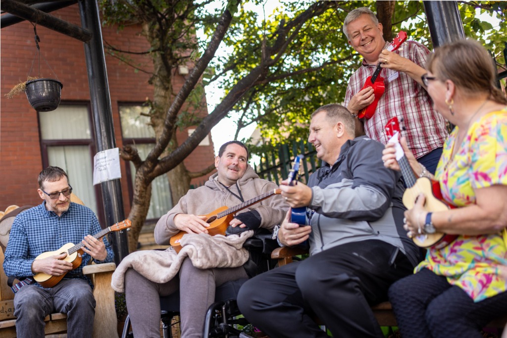 A group of men and women playing the ukulele in The Brain Charity garden